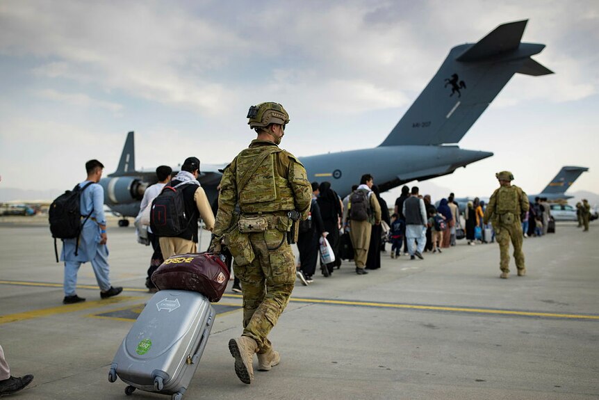 A soldier with a suitcase at an airport in a line of Afghan people.