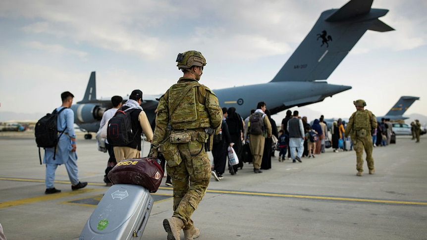 soldier with suit case wheels bag to airport with line of Afghan people