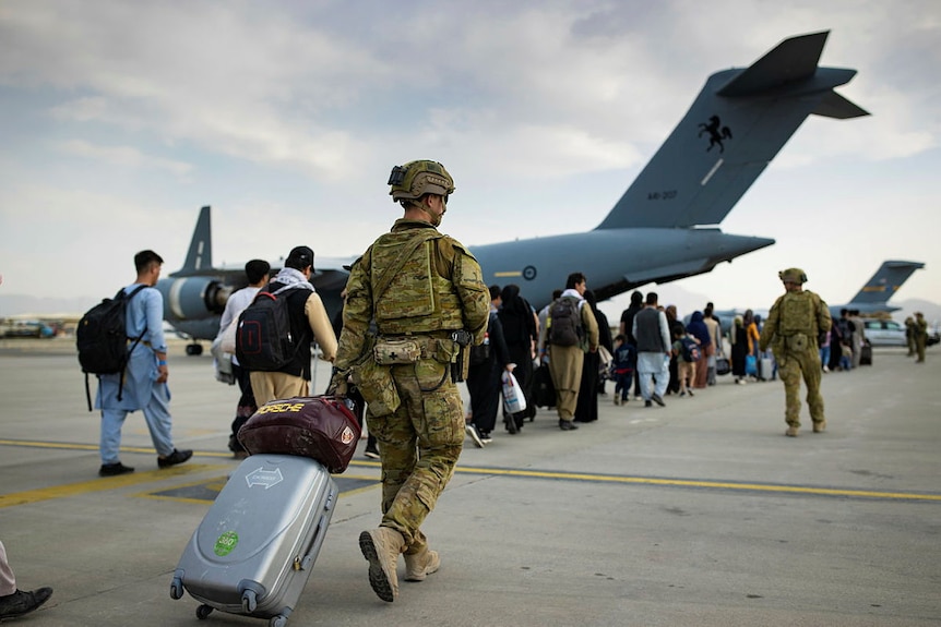 soldier with suit case wheels bag to airport with line of Afghan people