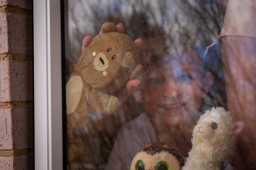 Seven-year-old James Pym is holding a teddy bear up to his window