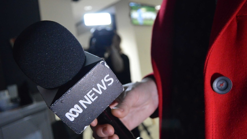 Hand holding ABC News microphone with camera blurred out in background.