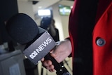 Hand holding ABC News microphone with camera blurred out in background.