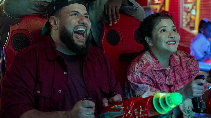 Mo plays an arcade shooting game with his on-screen girlfriend.