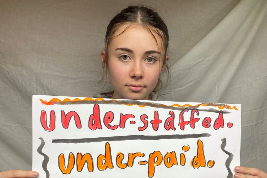 Teenage girl holds up her sign which reads 'under-staffed, under-paid, under-appreciated'. 