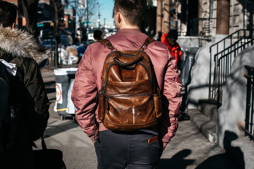 A man in New York wears a brown leather backpack.