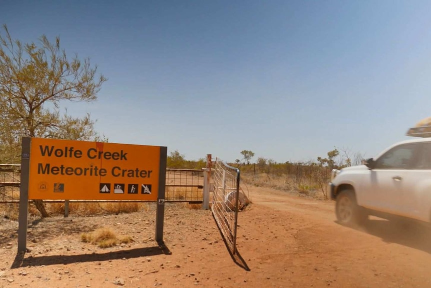 A car drives past the Wolfe Creek Meteorite Crater sign.