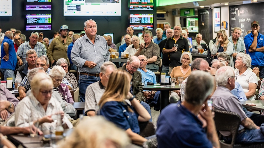 A man stands in a crowded room to ask a question.