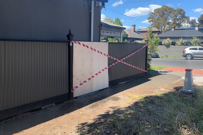 Fence with ply wood and red and white tape covering one panel.