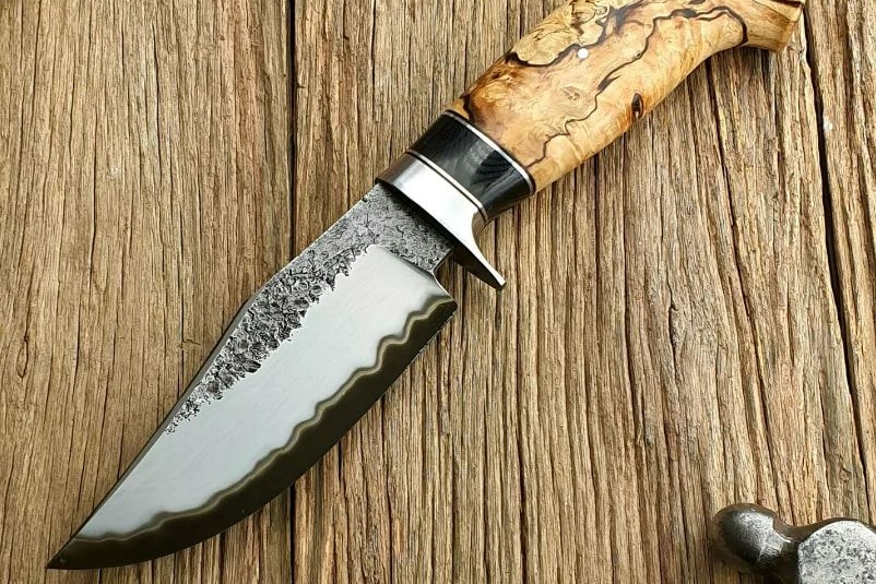A knife with a wooden handle and intricate metal design on the blade.