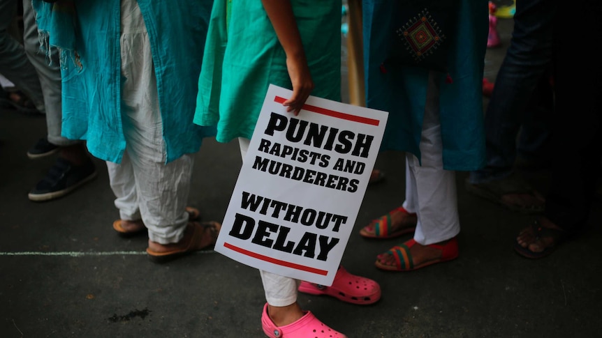 A woman is seen holding a sign with the phrase "punish rapists and murders without delays"