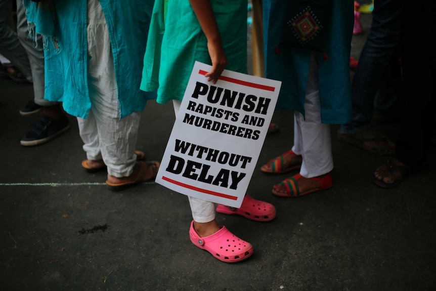 A woman is seen holding a sign with the phrase "punish rapists and murders without delays"