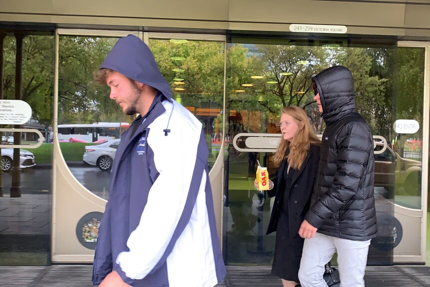 Two men in hoodies and a woman in front of sliding doors