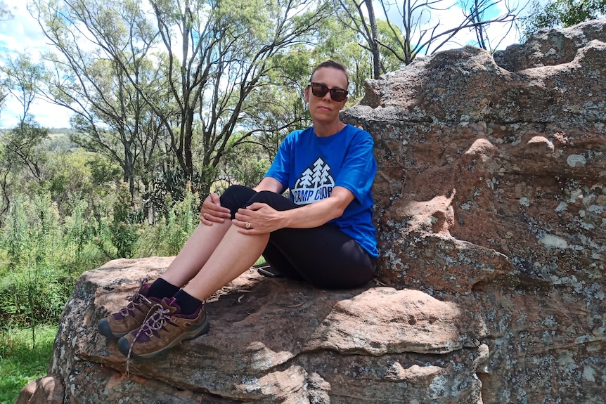 a woman sits on a large rock formation in the bush