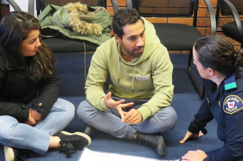 A young man and woman are sitting down talking to a female police officer in a room