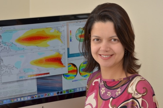 A woman sits in front of a computer screen. She is smiling.