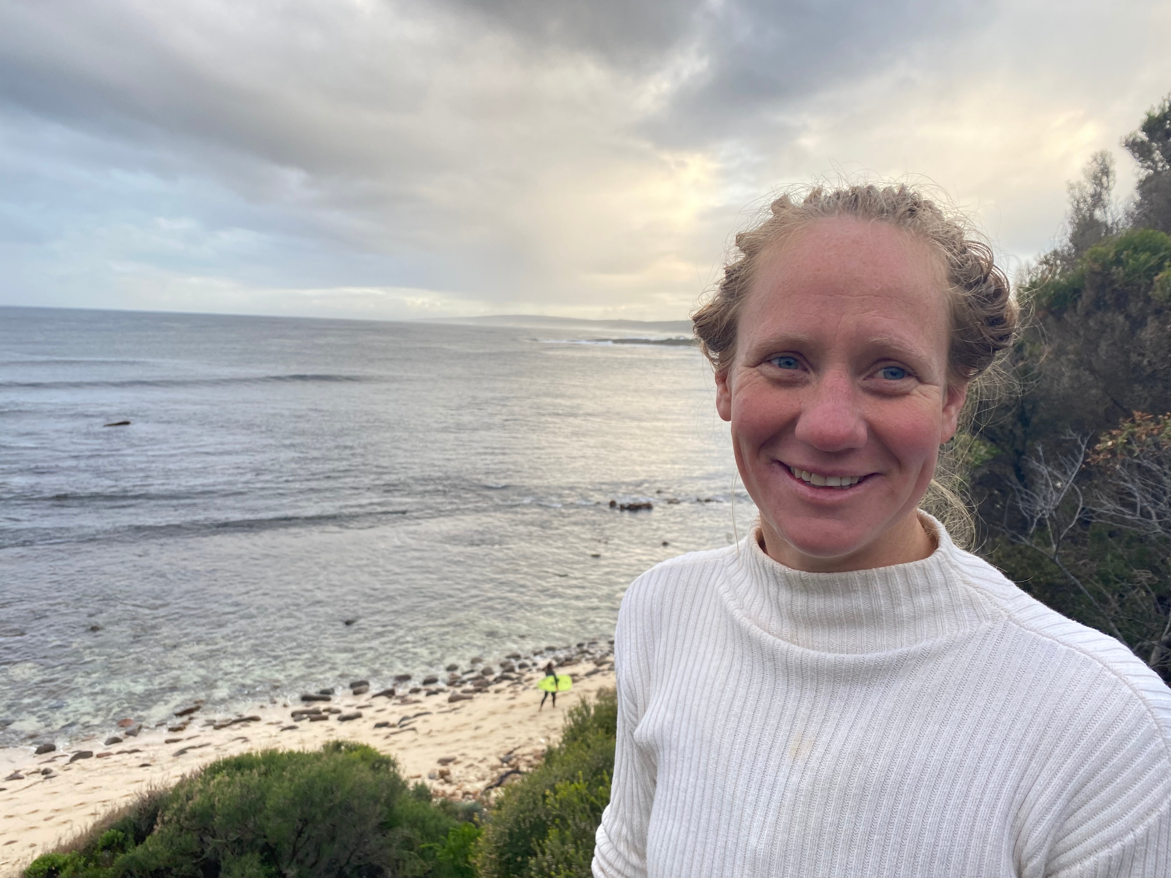 A woman in a white shirt with a beach in the background 