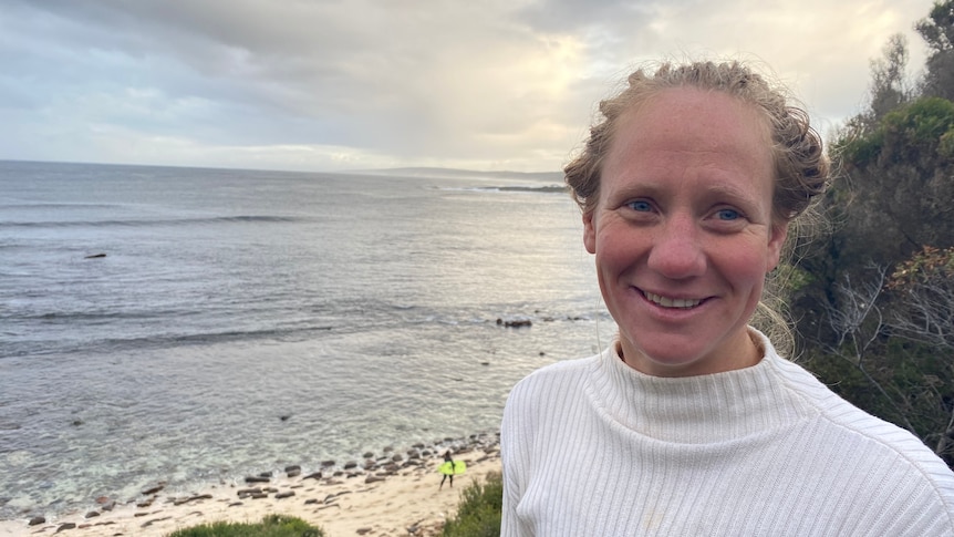 A woman in a white shirt with a beach in the background 