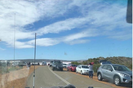 Cars parked next to the road at the Pink Lake as vehicles drive past.