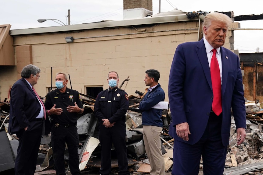 US President Donald Trump walks as Attorney-General William Barr speaks to police in front of a building damaged during protests