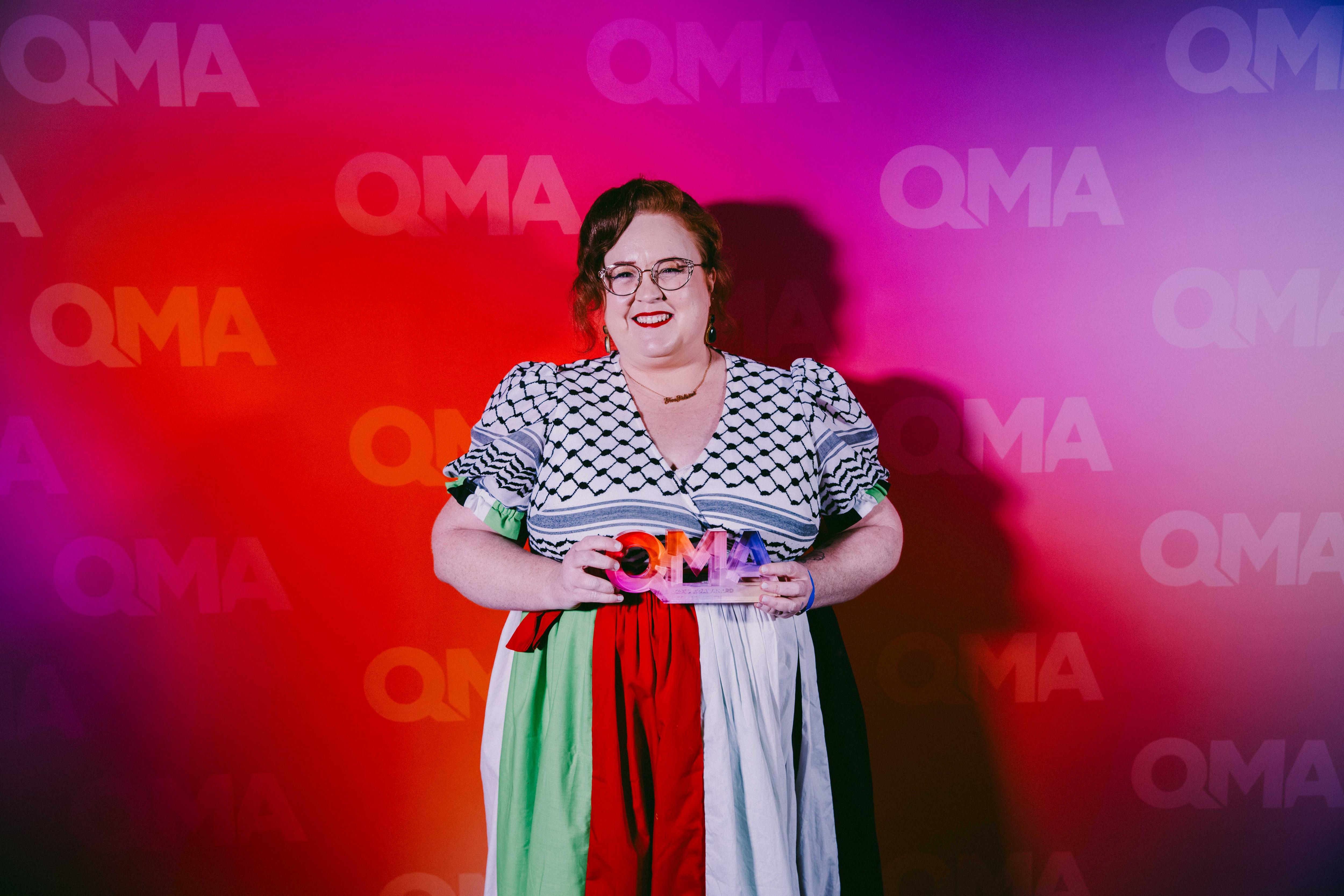 a woman wearing glasses smiles and holds an award trophy in her hands