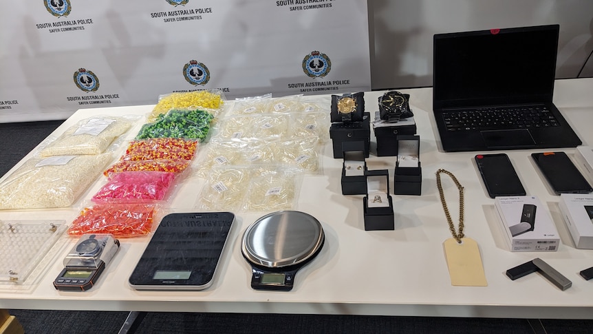 An array of items including jewellery, scales, a laptop, phones and what appears to be drugs in clear bags laid on a table