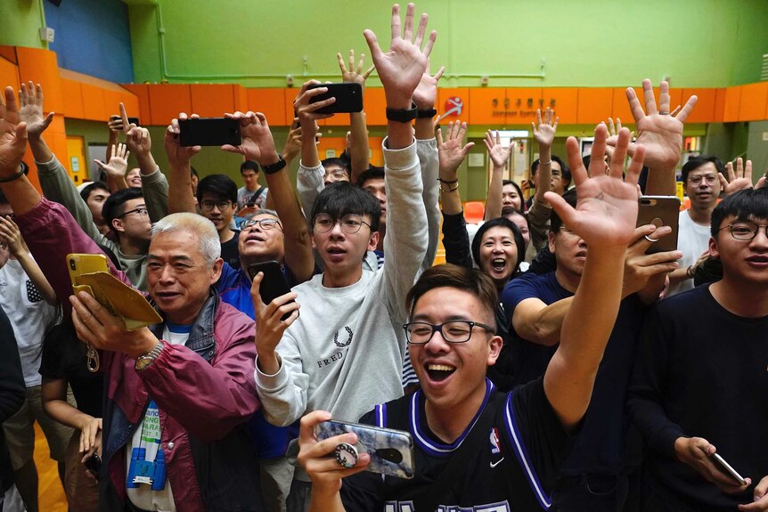 Dozens of pro-democracy supporters look happy and hold up their hands in celebration