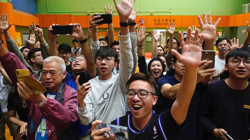 Dozens of pro-democracy supporters look happy and hold up their hands in celebration