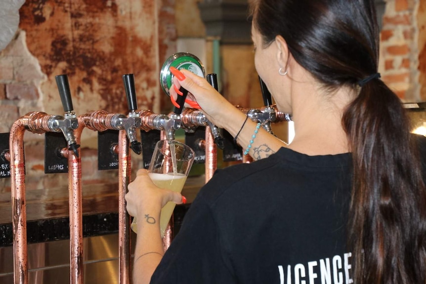 Taken from behind the bar, a female bartender pours a pint of tap beer.