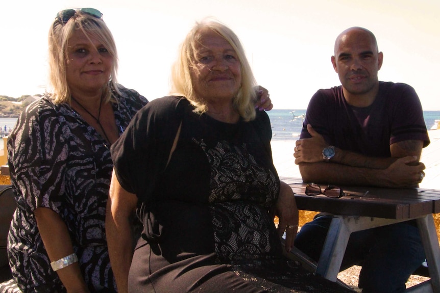 Two women and a man pose for a photo sitting at an outdoor picnic table.