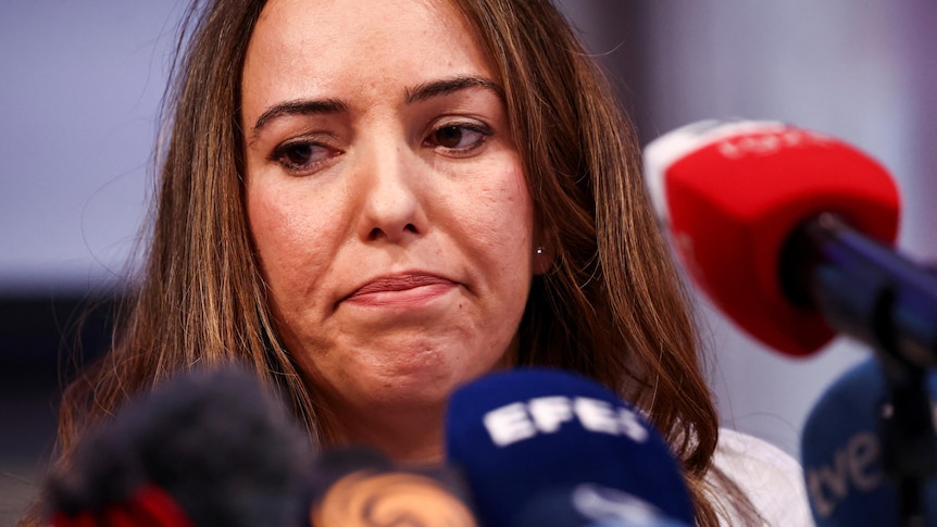 A woman with brown hair looks dejected while sitting at a news conference.