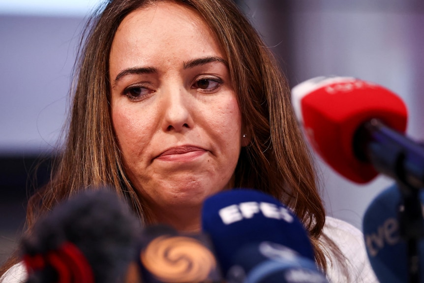 A woman with brown hair looks dejected while sitting at a news conference.