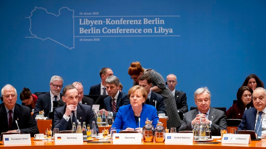 Looking at a warm, large orange desk in front of a blue background with various world leaders sitting behind the desk.