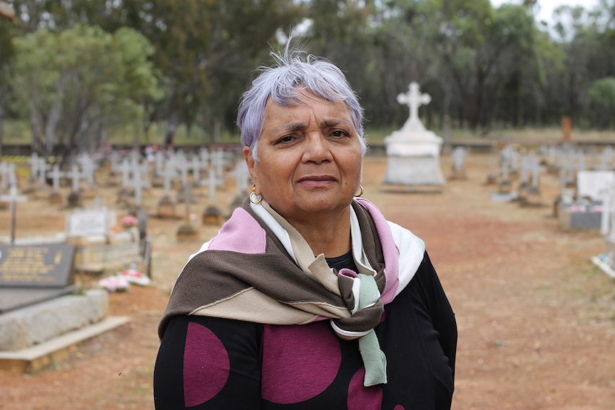 woman stands in front of cemetery, with headstones in the background