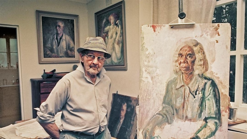 Australian artist Arthur Murch in his studio, standing next to a portrait of Rubina Namatjira on an easel