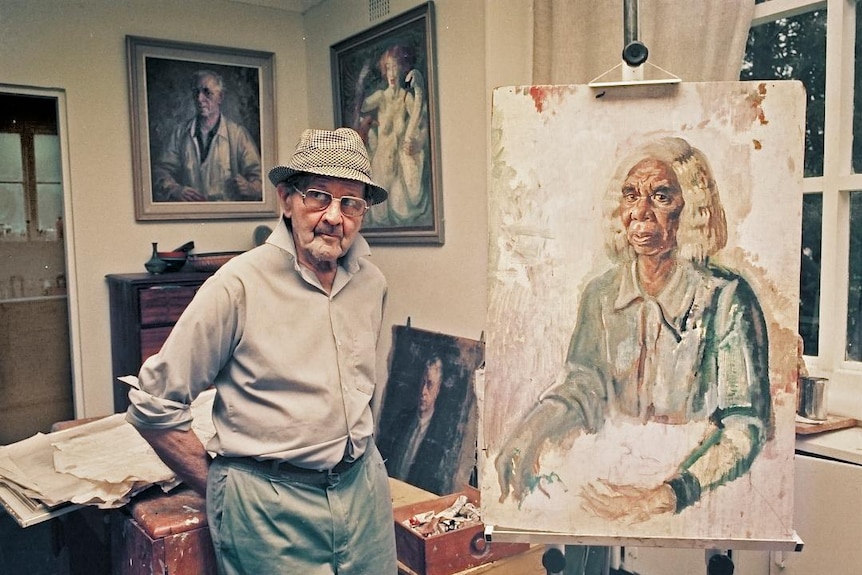 Australian artist Arthur Murch in his studio, standing next to a portrait of Rubina Namatjira on an easel