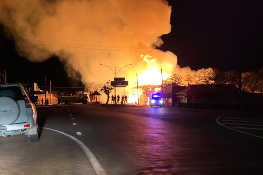 A street in a country town where a pub is engulfed in flames, locals looking on