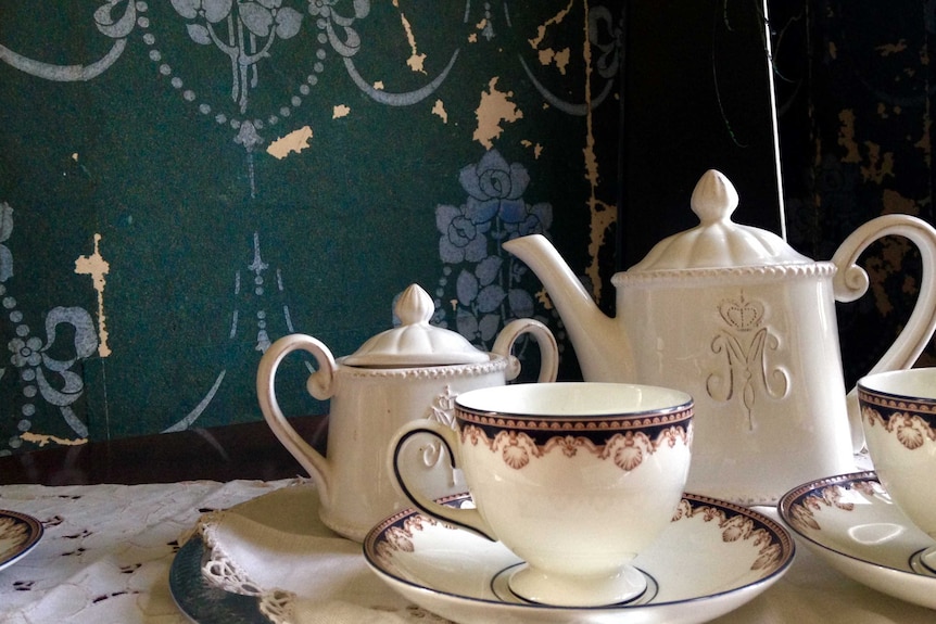 A white porcelain tea set, comprised of two cups and saucers and a teapot, on a white tablecloth.
