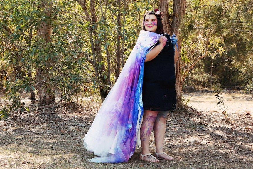 Kira Coleman smiles, wearing her trashed wedding dress like a cape