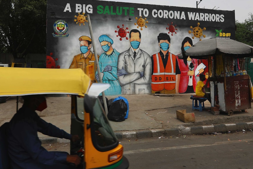 A yellow mini-taxi is about to drive past a colourful mural painted with medical staff wearing masks
