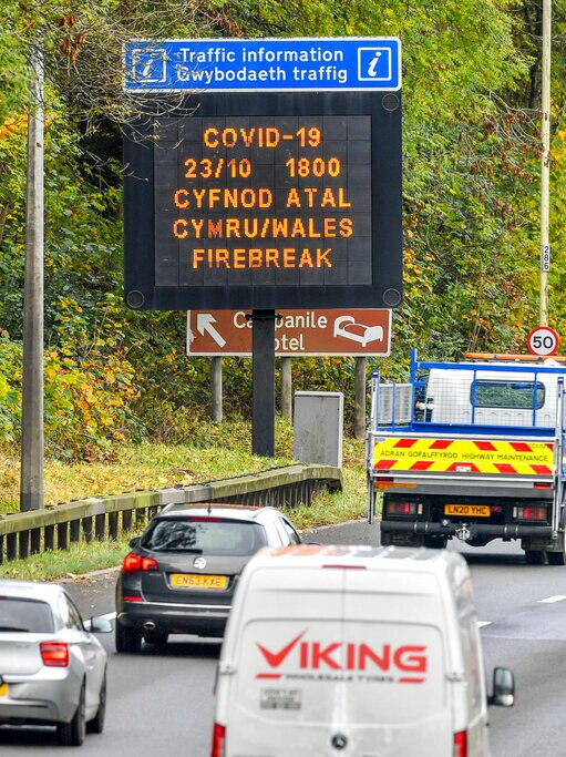 You view an aerial photo of a freeway with a black sign in Welsh and English warning motorists of COVID-19 restrictions.