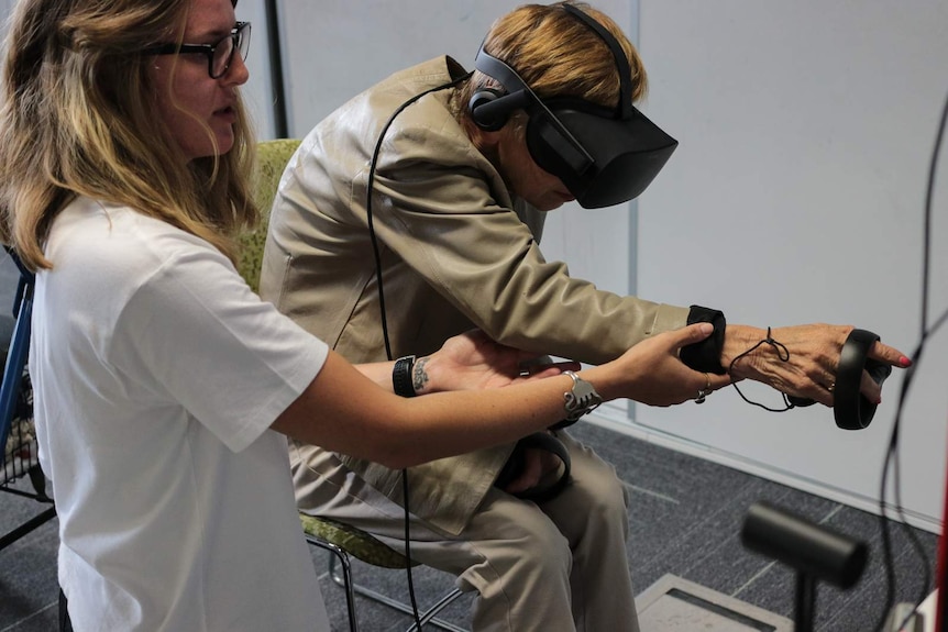 A woman assists an older woman to connect to a virtual reality headset.