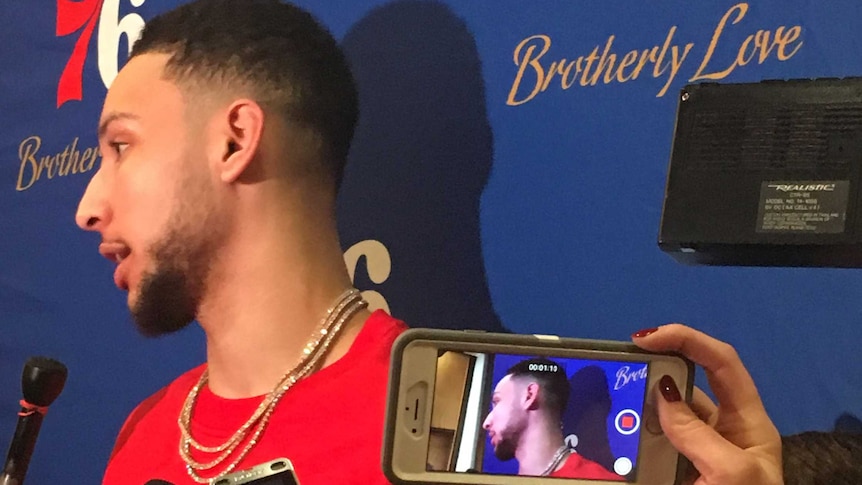 Ben Simmons faces a barrage of microphones and recording devices as he addresses the media after an NBA game