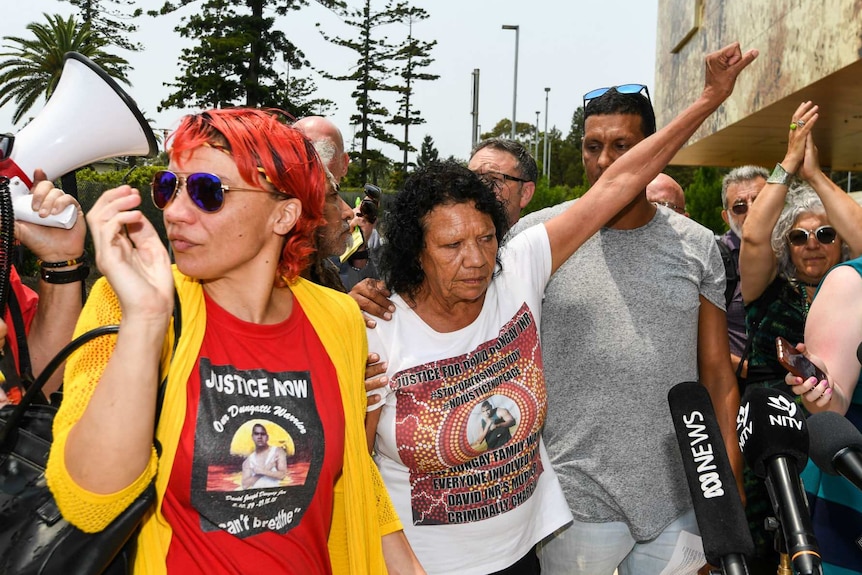 Two women are surrounded by supporters and news microphones.