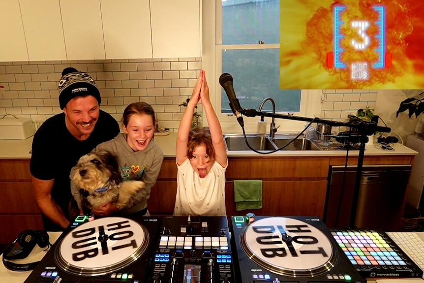 キッチンのビニール製の DJ デッキの周りで微笑む男性、子供 2 人、犬