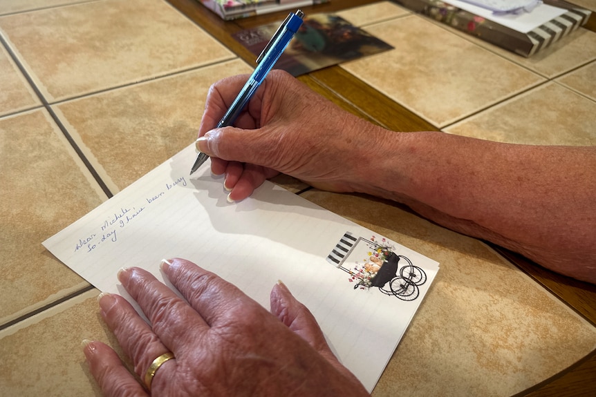 A woman hands writes a letter at a table