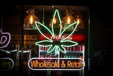 A neon sign shaped in the words Wholesale & Retail and a cannabis flower outside a shop window