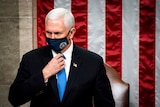 Mike Pence, wearing a mask with the seal of VP on it, stands in front of a US flag
