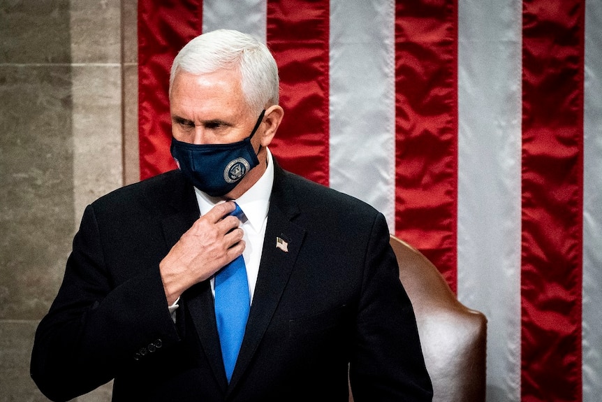 Mike Pence, wearing a mask with the seal of VP on it, stands in front of a US flag