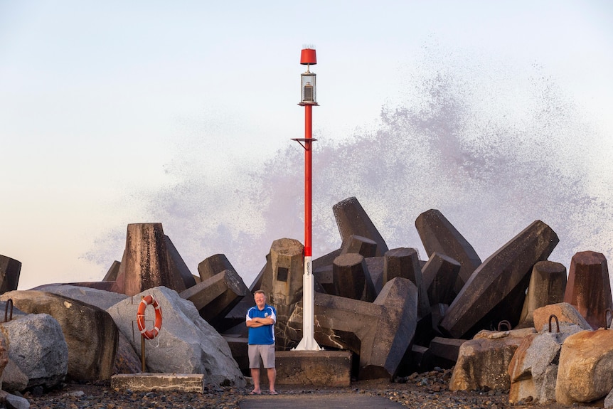 A man stands in front of the Narooma Bar, with a wave breaking in the background.