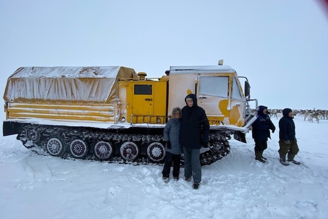 Four people stand near a large snowmobile truck